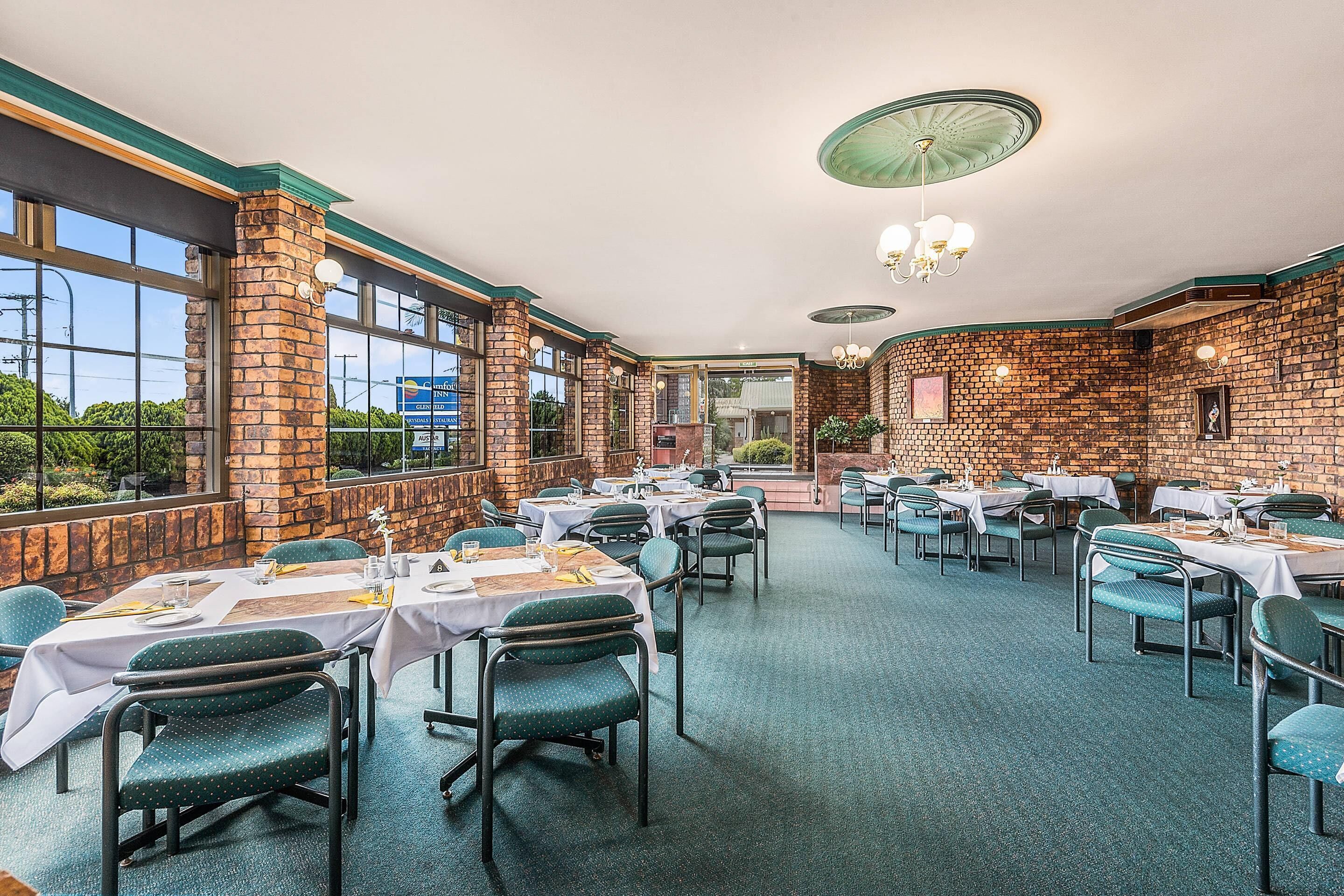 A restaurant with brick walls, large windows, and tables set for dining.