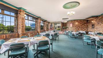 Un restaurant aux murs de briques, aux grandes fenêtres et aux tables dressées pour le service.