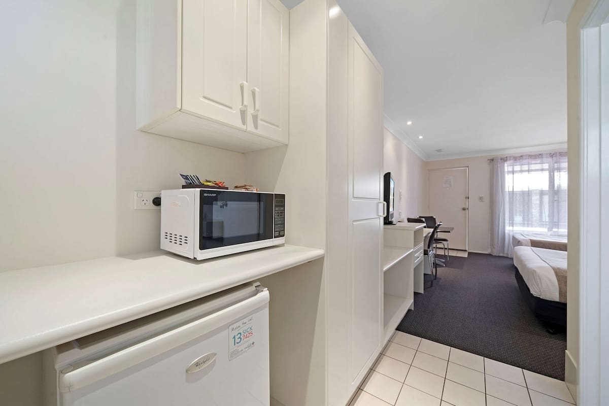 A compact hotel room with a kitchenette, a bed, a desk, and a chair.