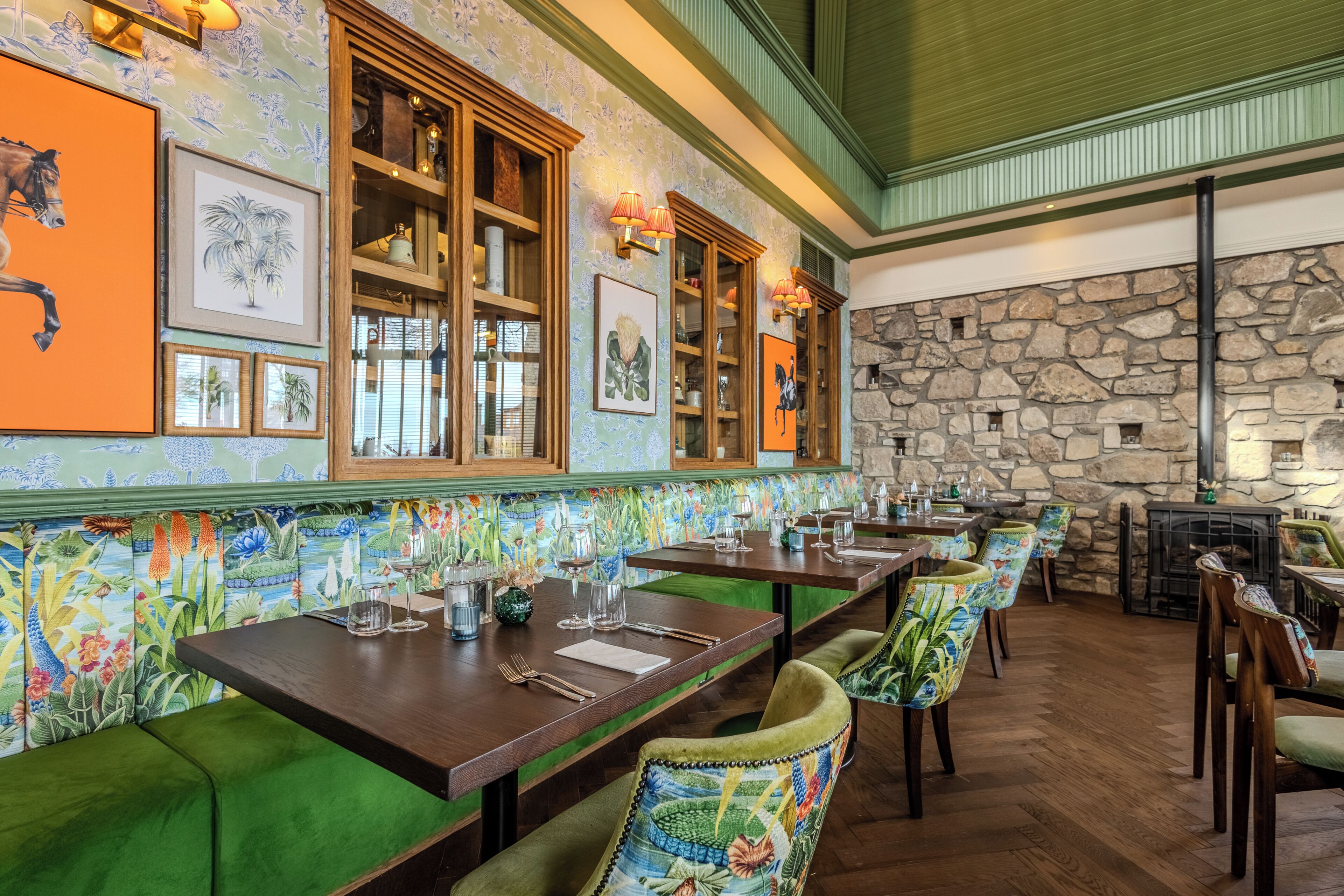 A restaurant with wooden tables, green cushioned benches, and a stone wall.