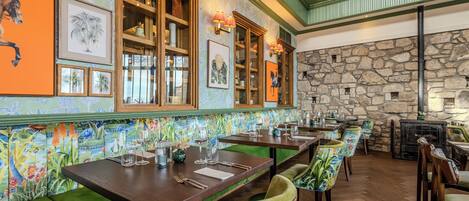 A restaurant with wooden tables, green cushioned benches, and a stone wall.