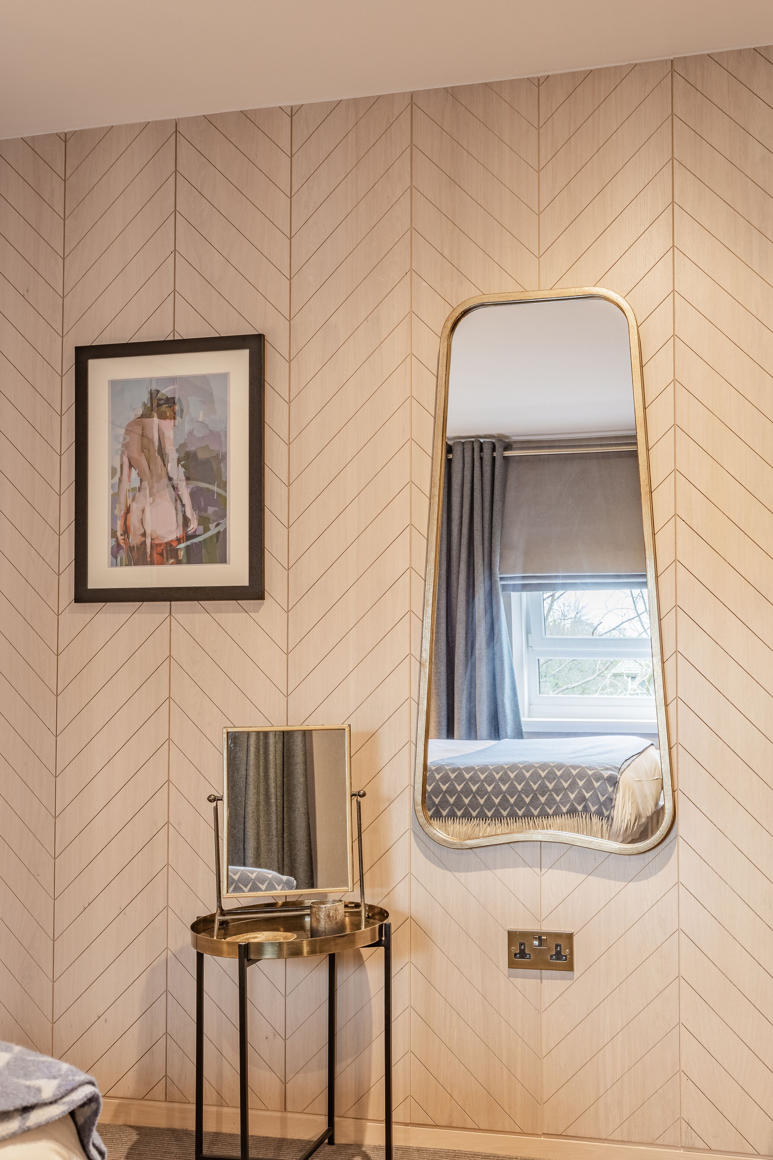 Una habitación con pared de diseño geométrico en forma de estampilla, una obra de arte en marco, un espejo y una ventana con cortinas.
