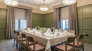 A dining room with a rectangular table set for a meal, surrounded by chairs, with a chandelier above.