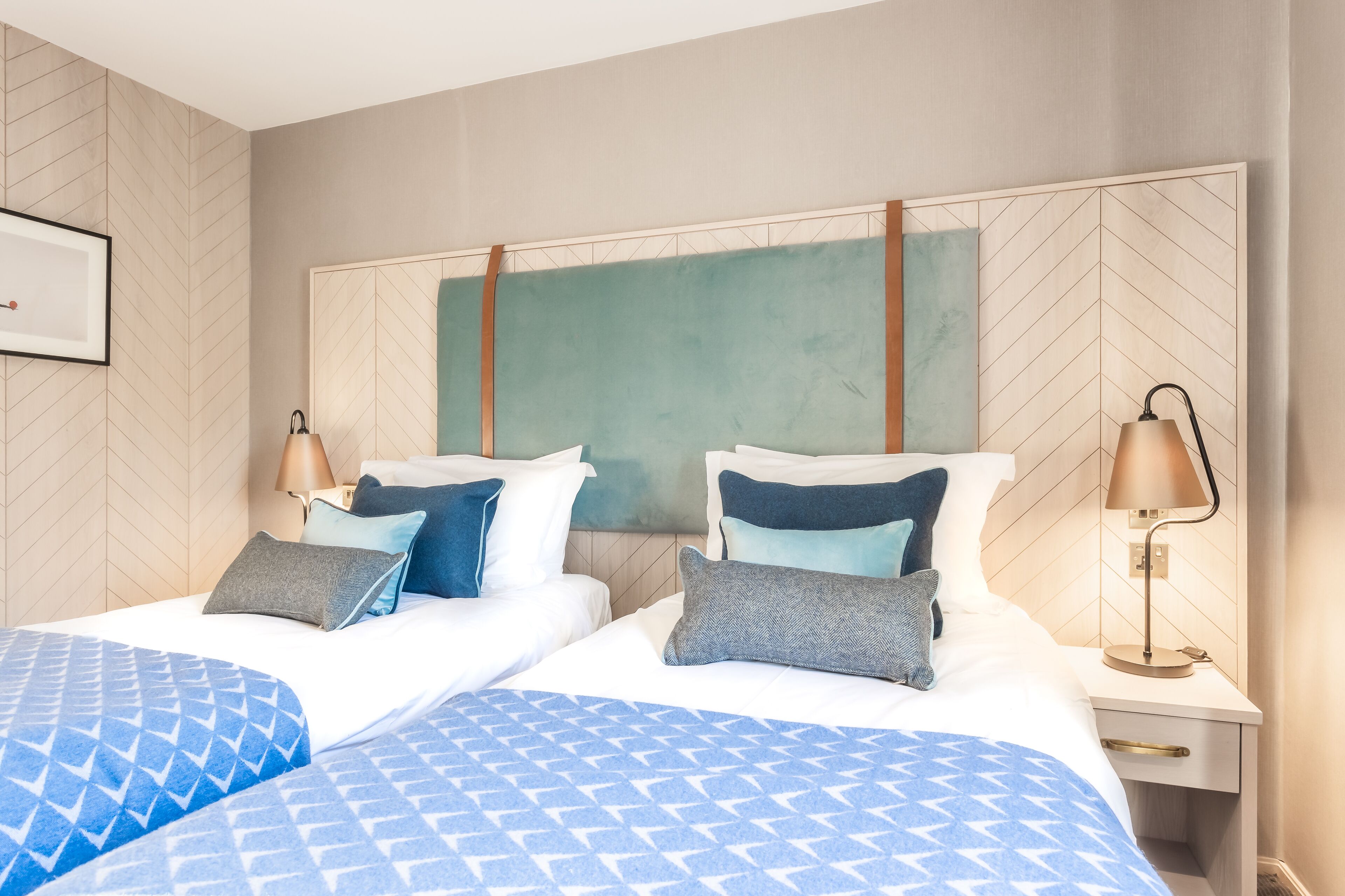 A hotel room with two beds, a nightstand with a lamp, and a large wall-mounted artwork.
