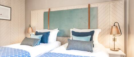 A hotel room with two beds, a nightstand with a lamp, and a large wall-mounted artwork.