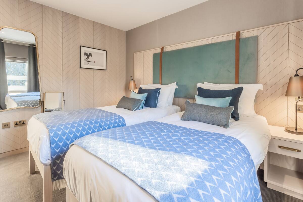 Une chambre d’hôtel avec deux lits, un grand miroir, un tableau encadré et une table de chevet avec une lampe.