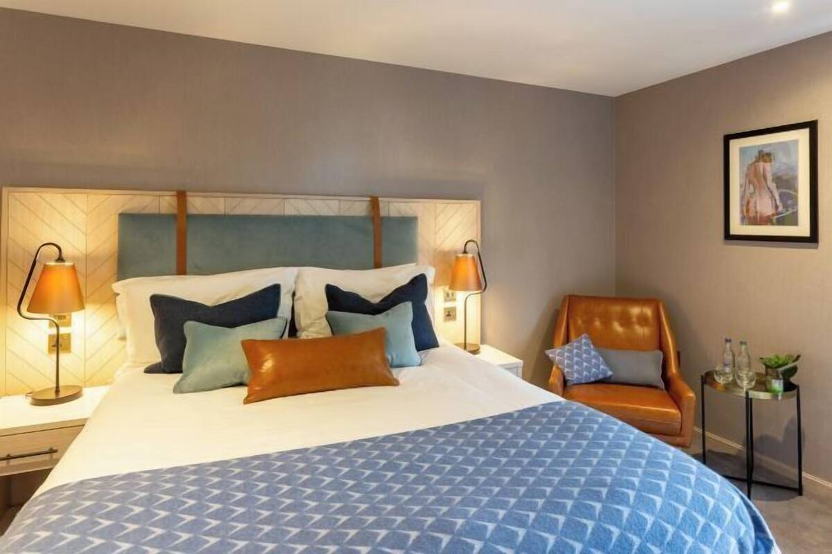 Une chambre d’hôtel avec un grand lit, deux lampes de chevet, une chaise et une petite table sur laquelle est posée une plante.