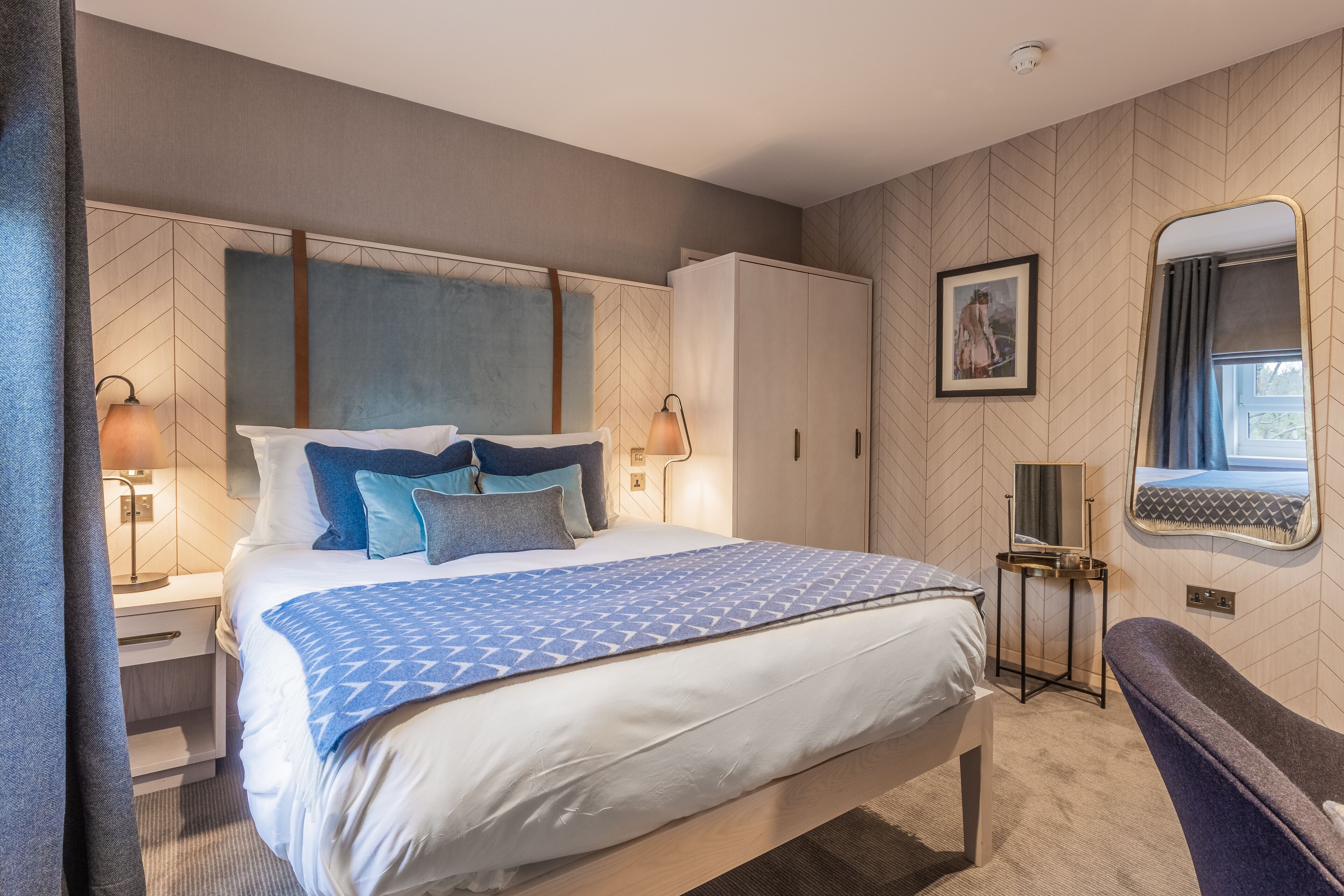 Quarto de hotel moderno com uma cama grande, um guarda-roupa, mesa de cabeceira com luminárias, espelho e janela com cortinas.