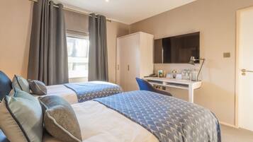 A hotel room with two beds, a desk, a TV, and a wardrobe.