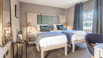 A hotel room with two beds, a desk, a chair, a mirror, and a window with curtains.