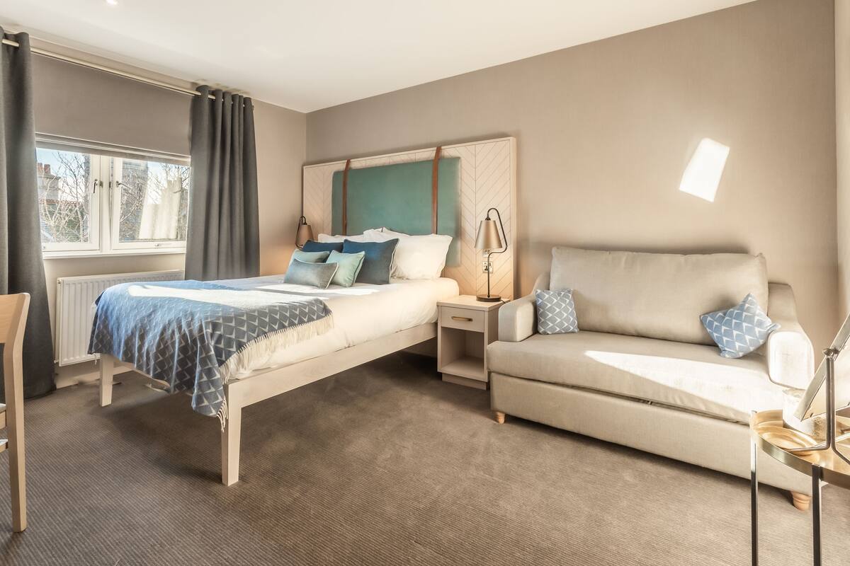 Une chambre à coucher avec un lit, un canapé, une table de chevet et une lampe.