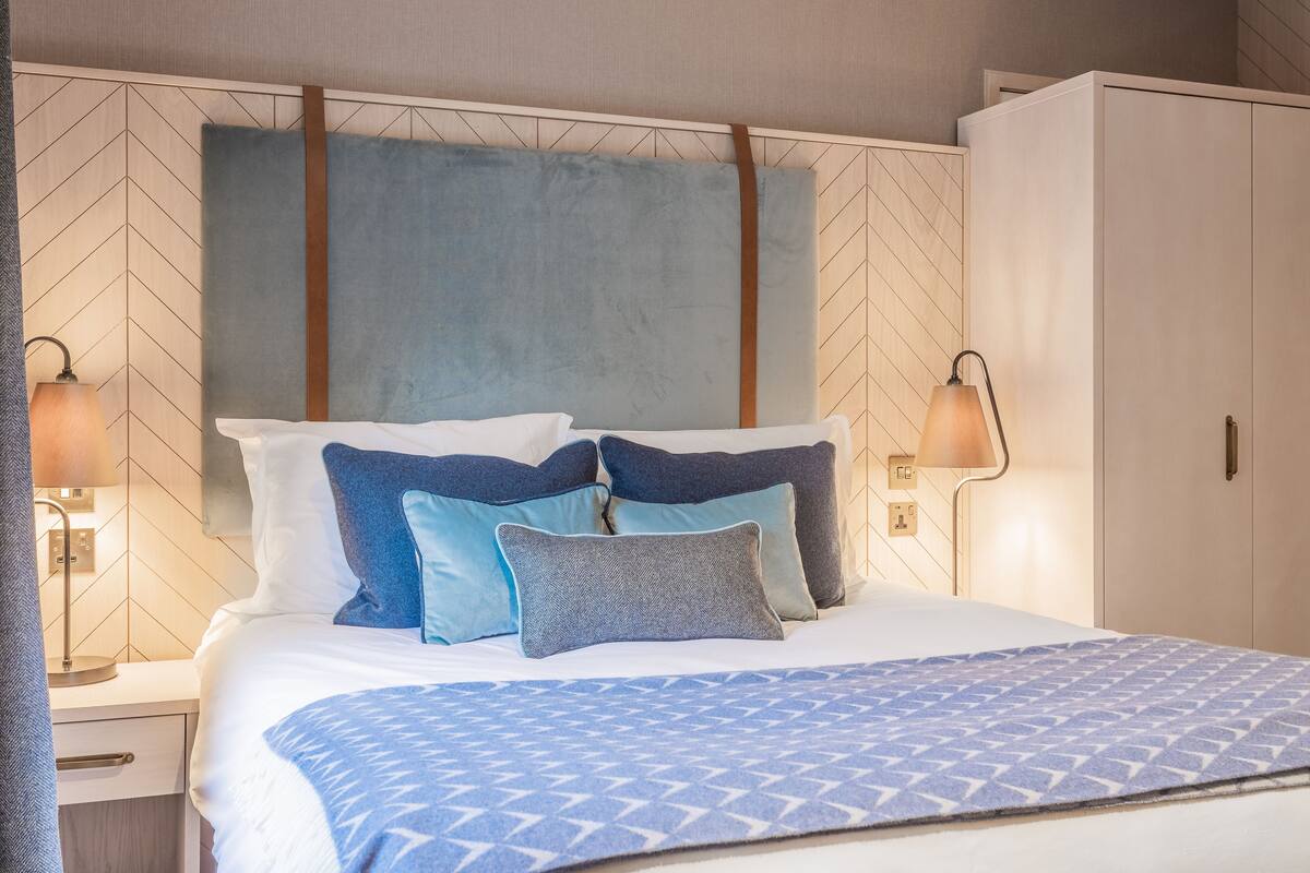 Un lit bien fait, recouvert d’une couvre-lit à motifs, avec deux lampes de chevet et une armoire dans une chambre d’hôtel.