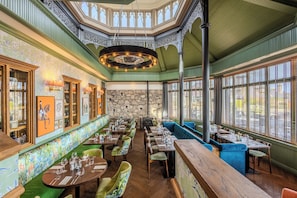 A restaurant with a high ceiling, ornate ceiling design, stone wall, and large windows. - Palm Court Hotel (Aberdeen)