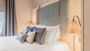 A neatly made bed with multiple pillows, a headboard with a geometric pattern, and a bedside lamp.