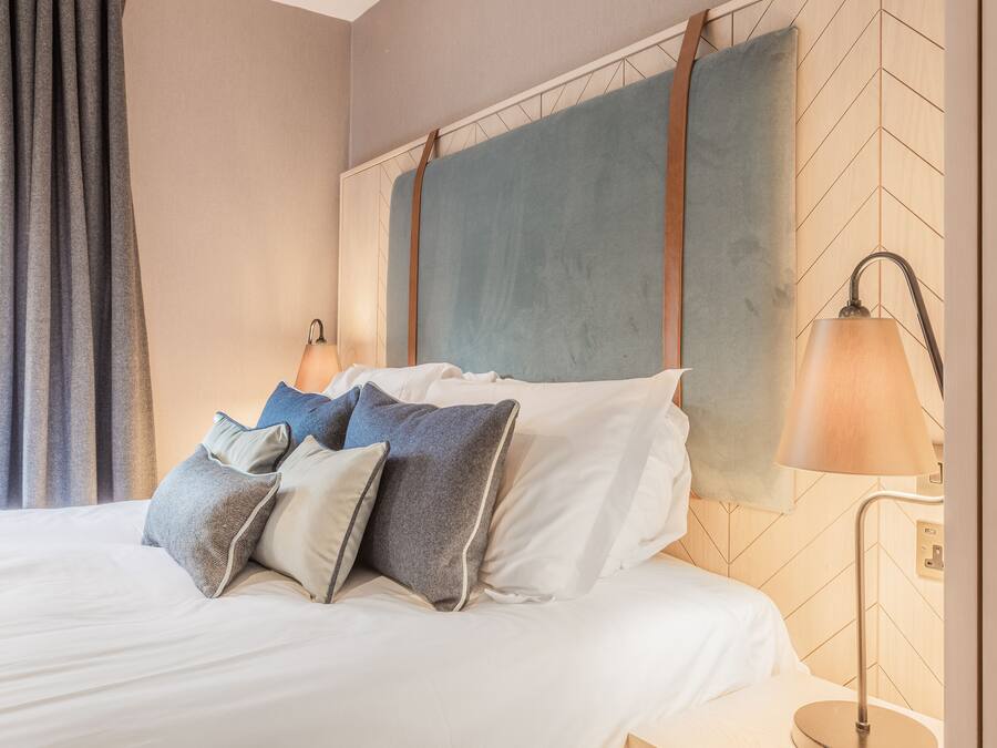 A neatly made bed with multiple pillows, a headboard with a geometric pattern, and a bedside lamp.
