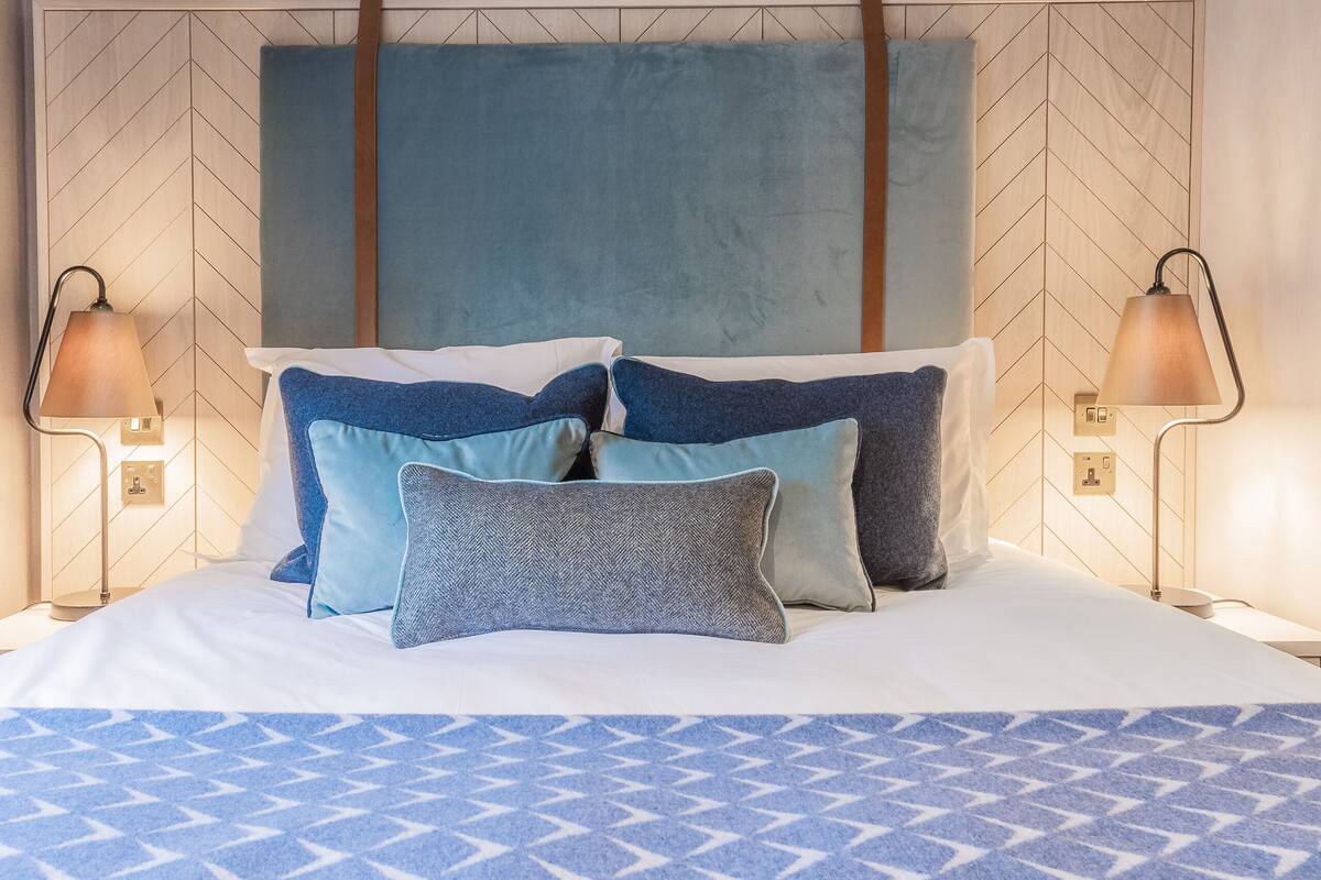 Un lit bien fait, avec une literie bleue et blanche, deux lampes de chevet et un mur orné d’un motif en chevrons.