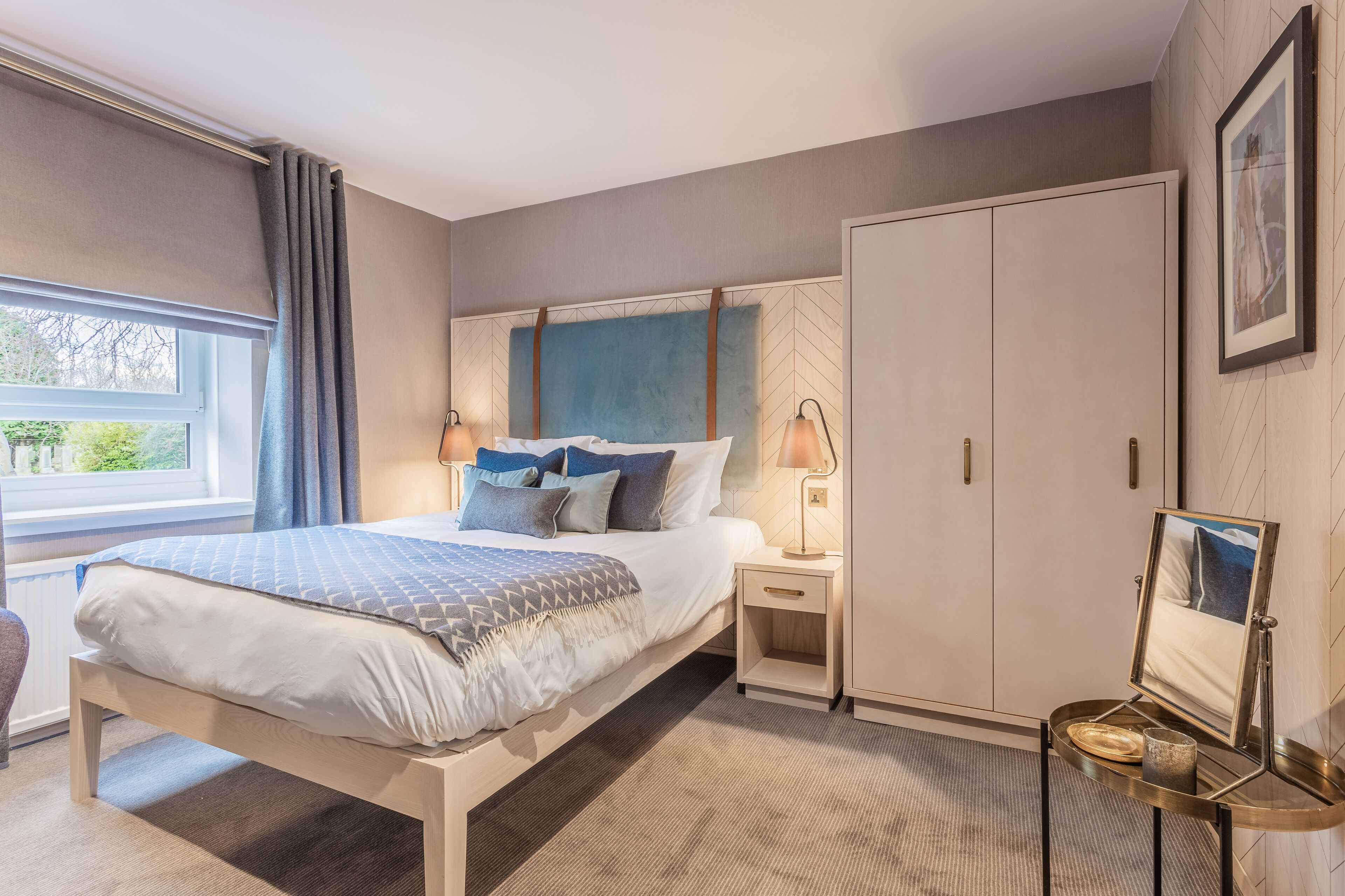 Quarto com cama, mesas de cabeceira, guarda-roupa e janela com cortinas.
