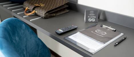 Un comptoir d’accueil d’hôtel avec un porte-bagages, un panneau « interdiction de fumer », une télécommande, un stylo et un document.