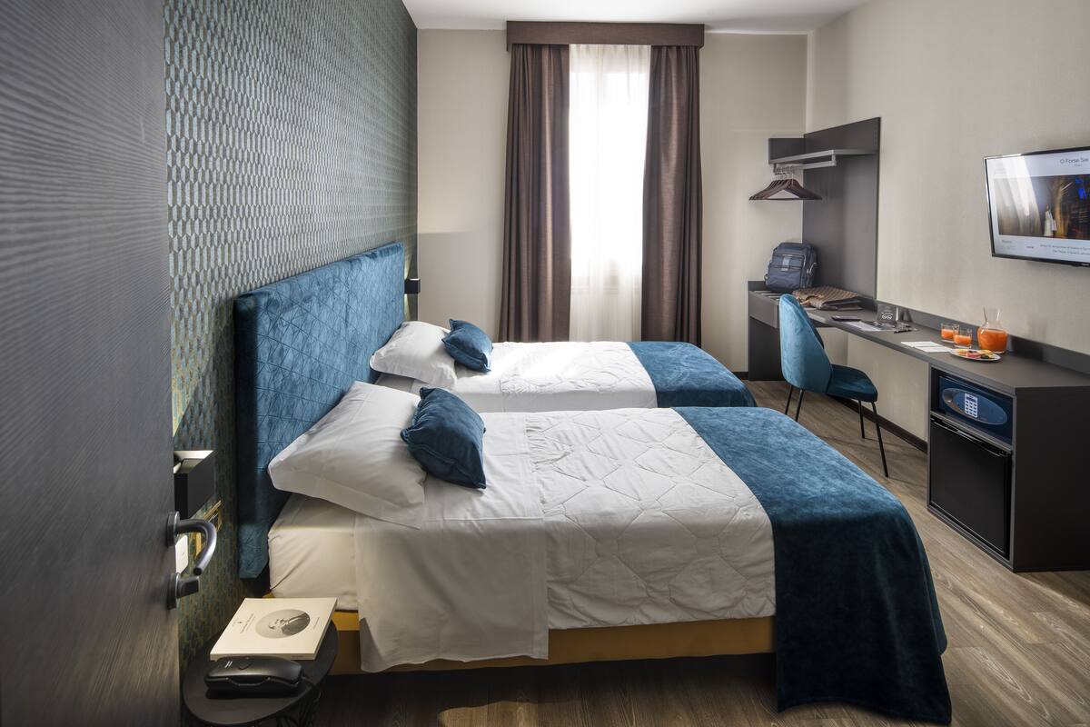 Une chambre d’hôtel avec deux lits, un bureau, une chaise, une télévision et une fenêtre avec des rideaux.
