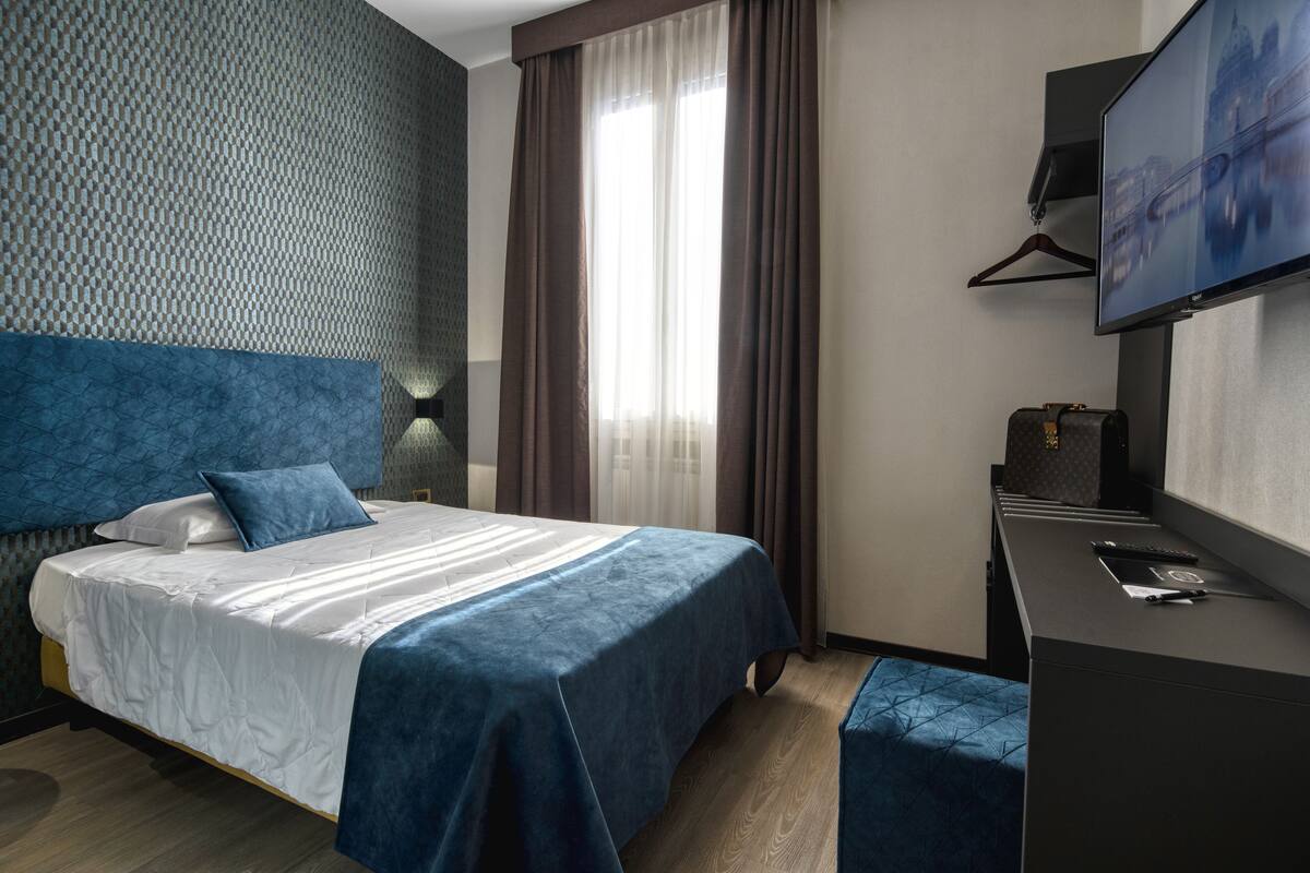 Une chambre d’hôtel avec un lit, un bureau, une télévision et une fenêtre avec des rideaux.