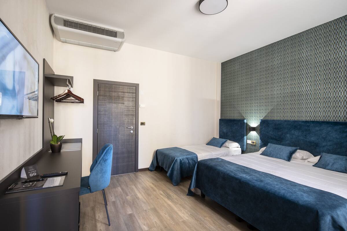 Une chambre d’hôtel moderne équipée de deux lits, d’un bureau, d’une chaise, d’une armoire et d’un climatiseur fixé au mur.