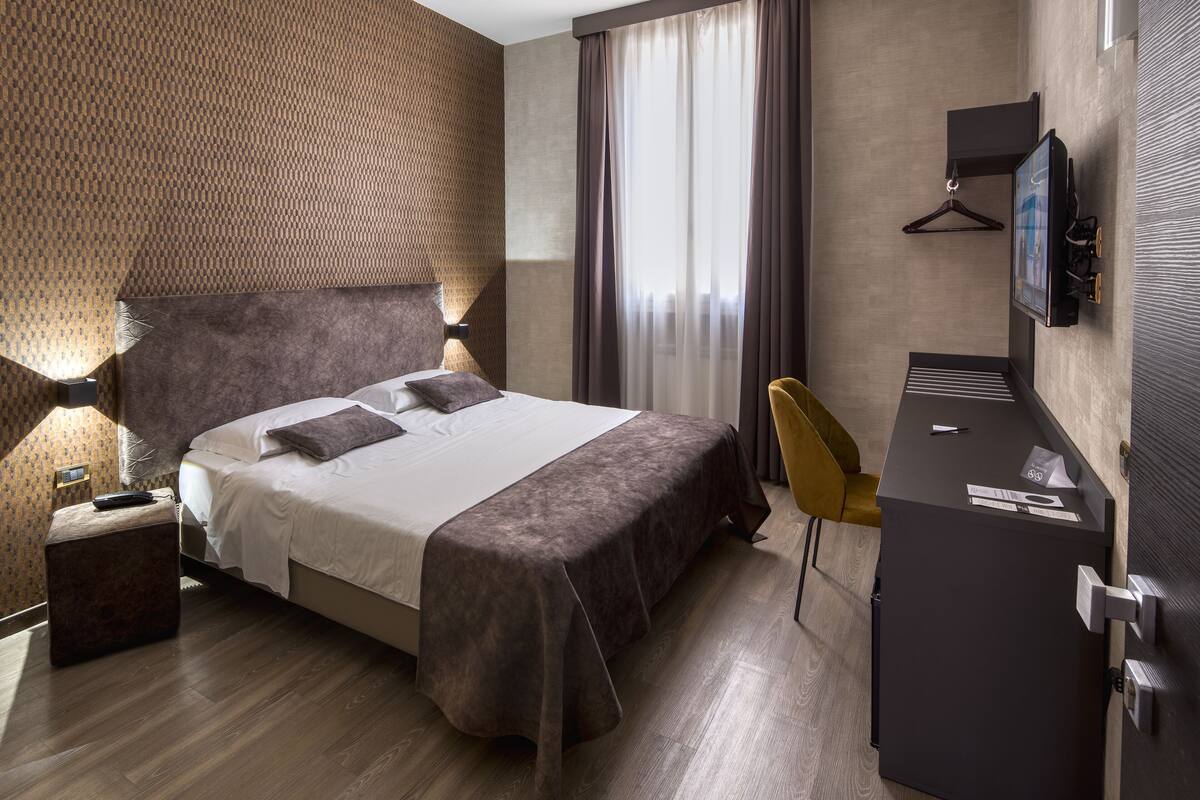 Une chambre d’hôtel avec un grand lit, des lampes de chevet, un bureau avec une chaise, une télévision et un porte-manteau.