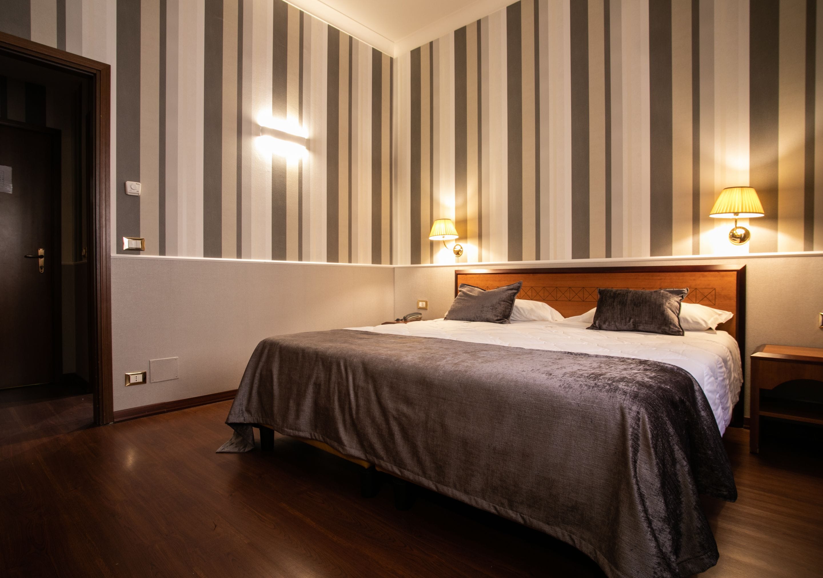 Una camera d'albergo con un letto grande, carta da parati a righe e due lampade sui comodini.