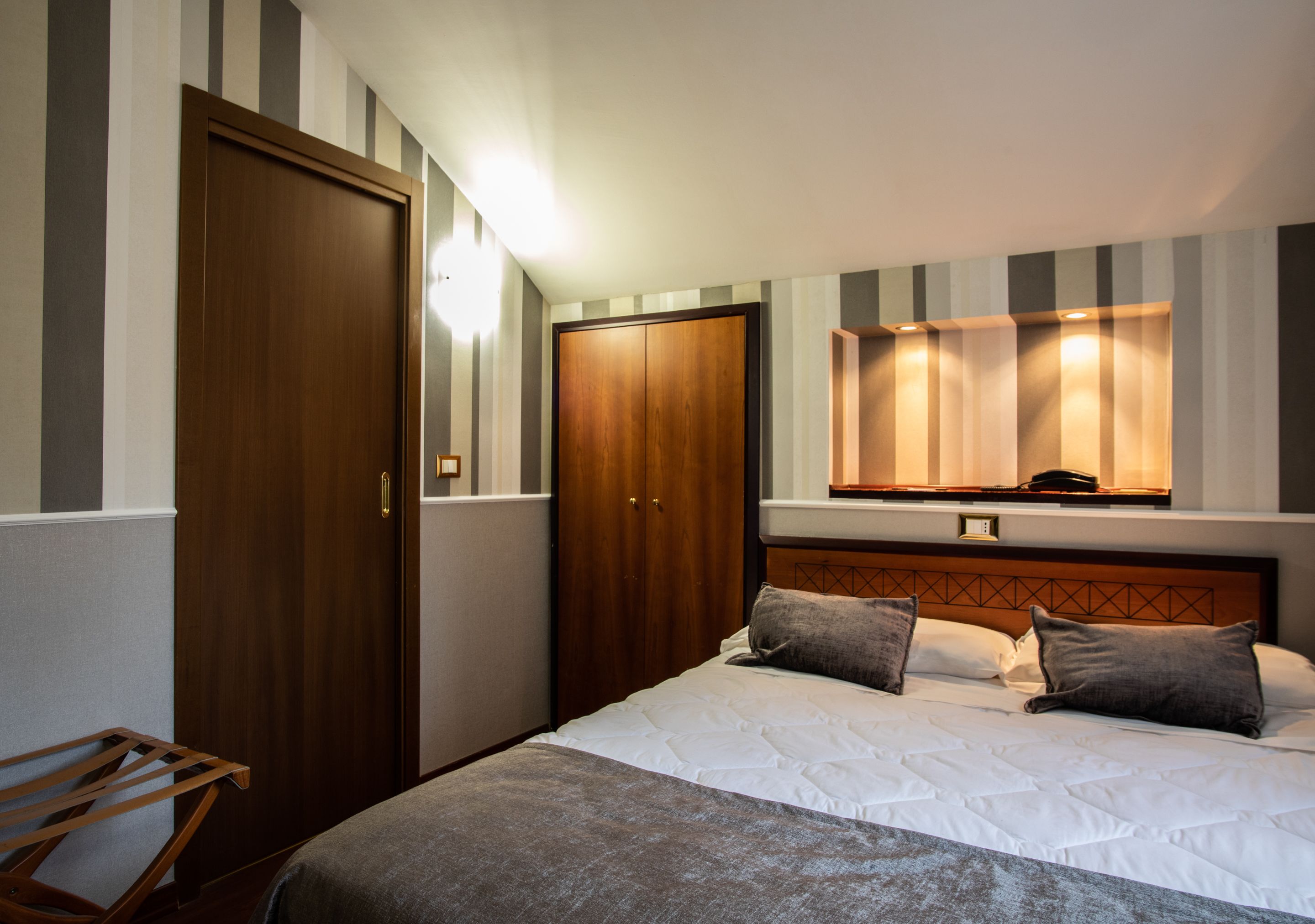 A hotel room with a bed, a wooden wardrobe, a mirror, and a small table.
