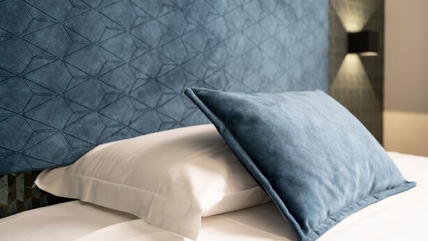 A bed with a geometric-patterned headboard and two pillows, one white and one blue. - Hotel Astoria (Bologna)
