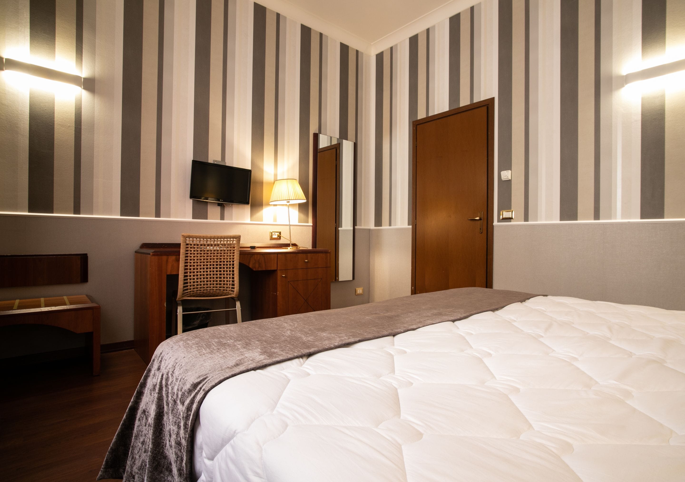 Una habitación de hotel con cama, escritorio, silla, televisión y puerta.
