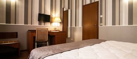 Una habitación de hotel con cama, escritorio, silla, televisión y puerta.