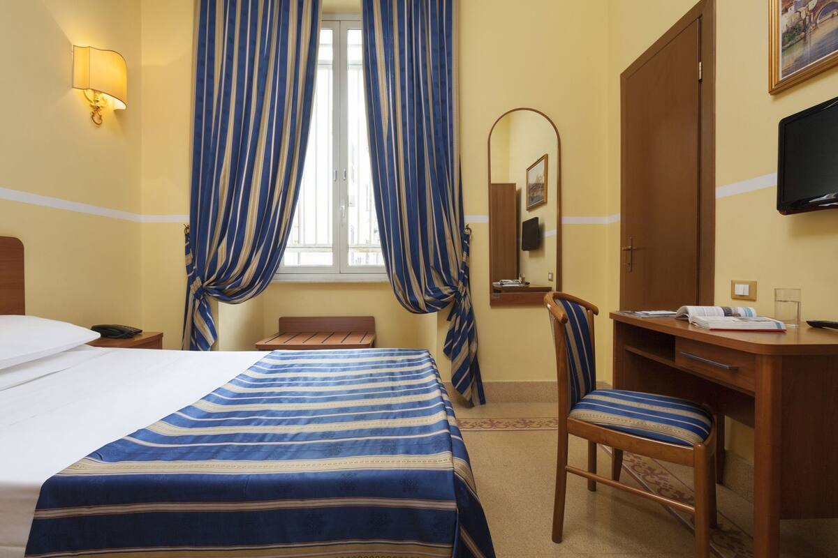 Una habitación de hotel con cama, escritorio, silla, espejo y televisor.