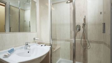 Un bagno moderno con doccia vetrata, lavandino bianco con specchio e pareti rivestite di piastrelle color crema.