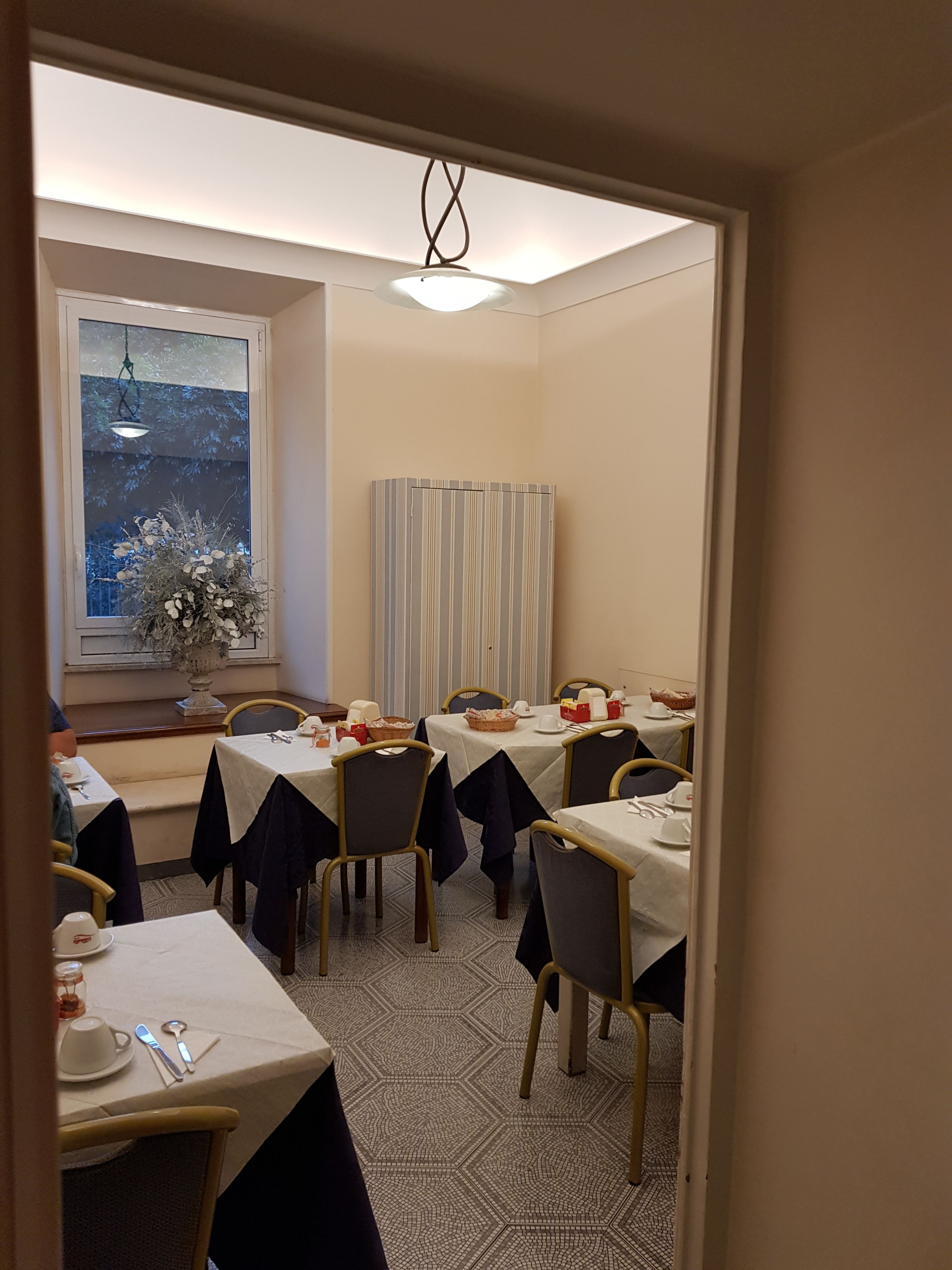 Un comedor con mesas listas para el servicio, una ventana con vistas y una planta decorativa.