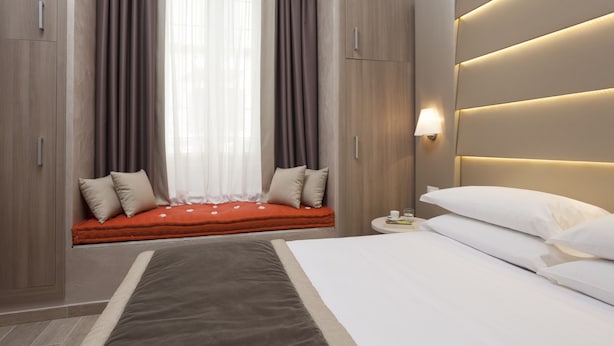 Una habitación de hotel moderna con una cama grande, una mesita de noche con lámpara, una ventana con cortinas y armarios empotrados.