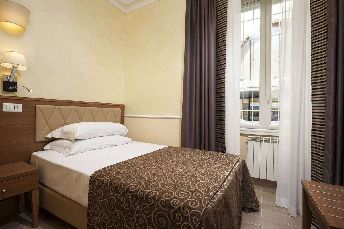 A hotel room with a bed, nightstand, and lamp.
