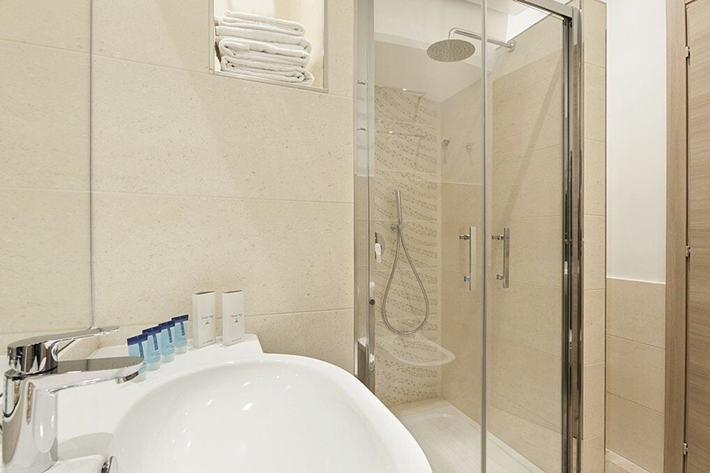 A modern bathroom with a large white sink, a glass shower enclosure, and neatly folded towels on a shelf.