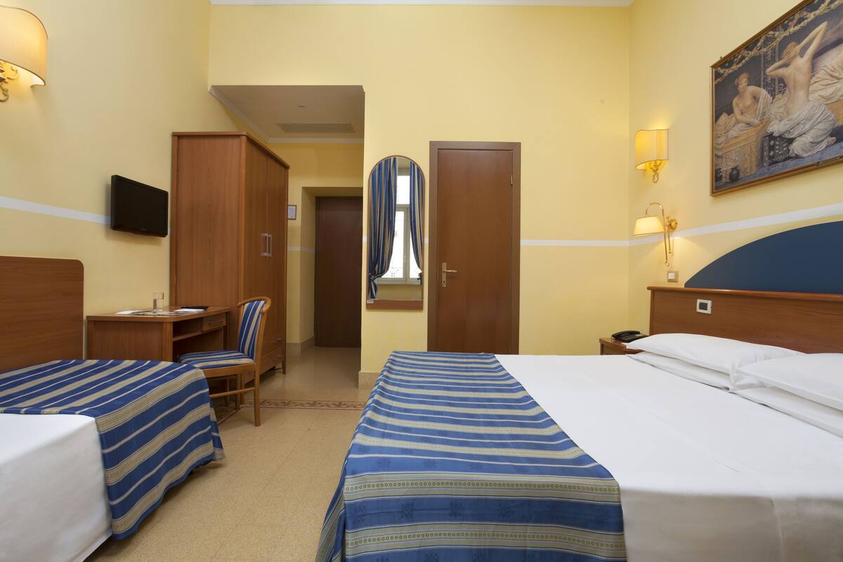 A hotel room with two beds, a desk, a chair, and a TV.
