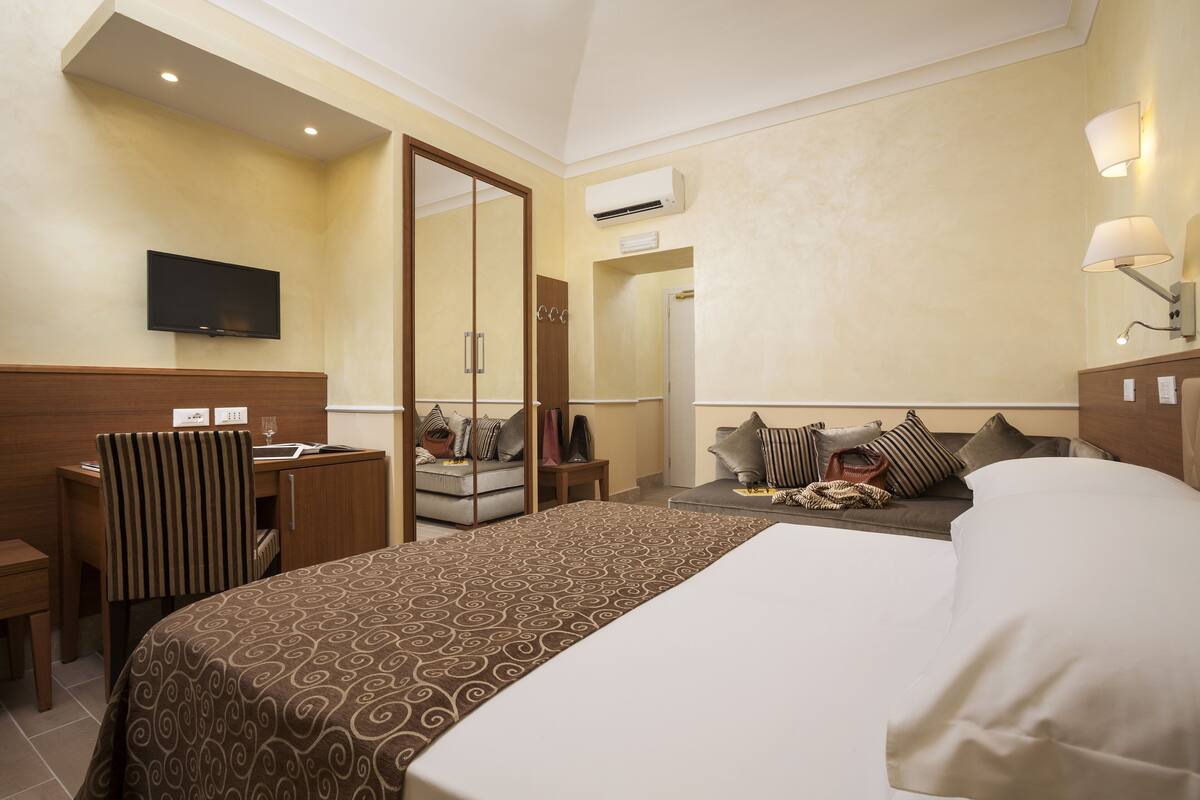 A hotel room with a bed, a desk, a chair, a TV, and a sofa.