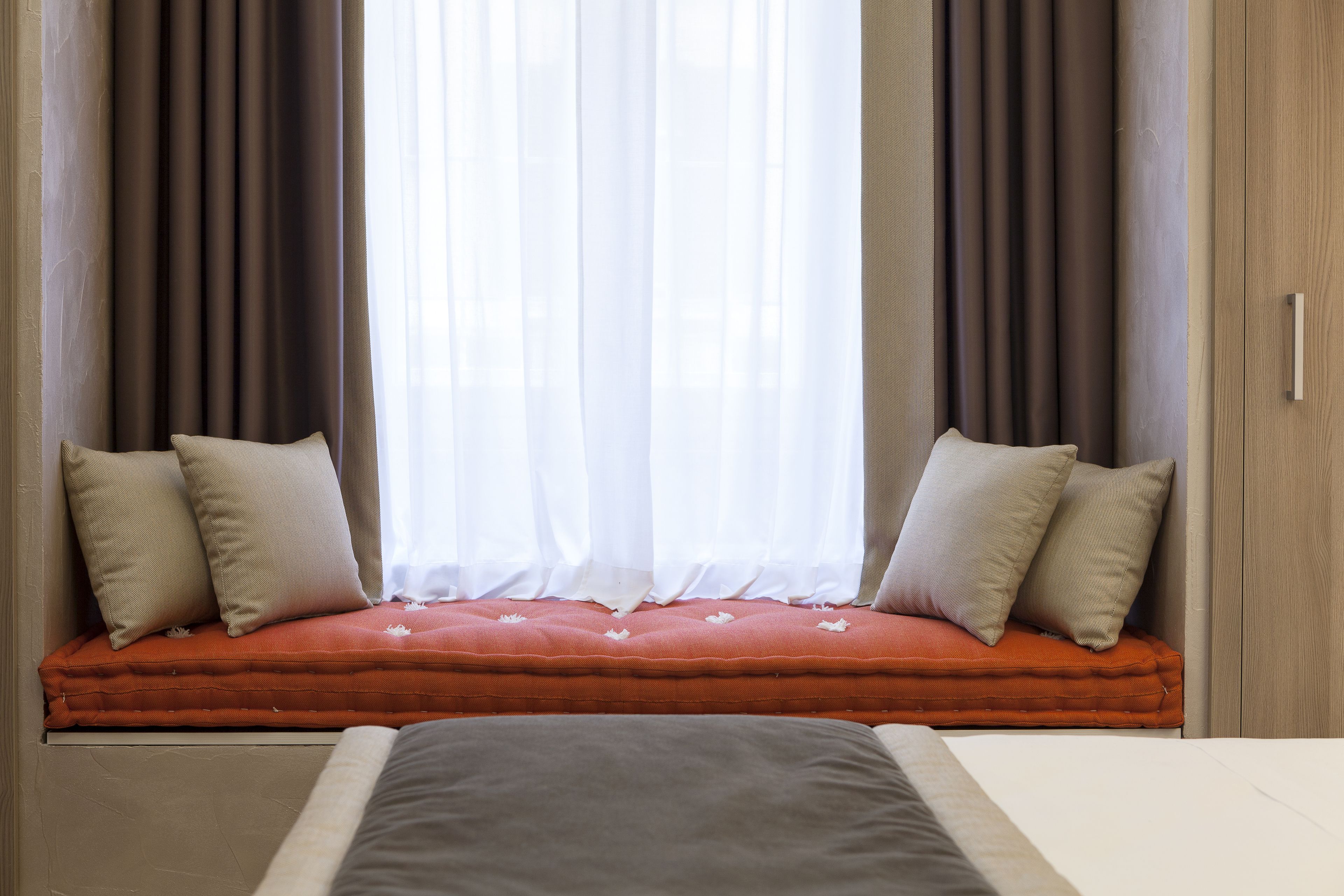 A bedroom with a bed, a window seat with cushions, and curtains.