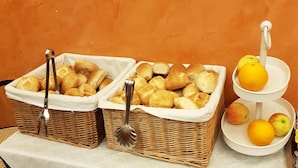 Una mesa de buffet con panes en cestas y una presentación de frutas.
