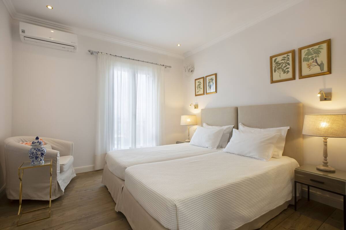 A hotel room with two beds, a sitting area with a chair, a small table, and a decorative vase.