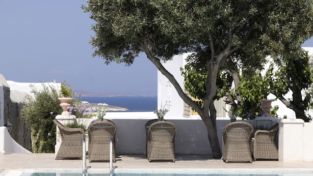 Ein Poolbereich mit Korbstühlen, einem Baum und Blick aufs Meer.