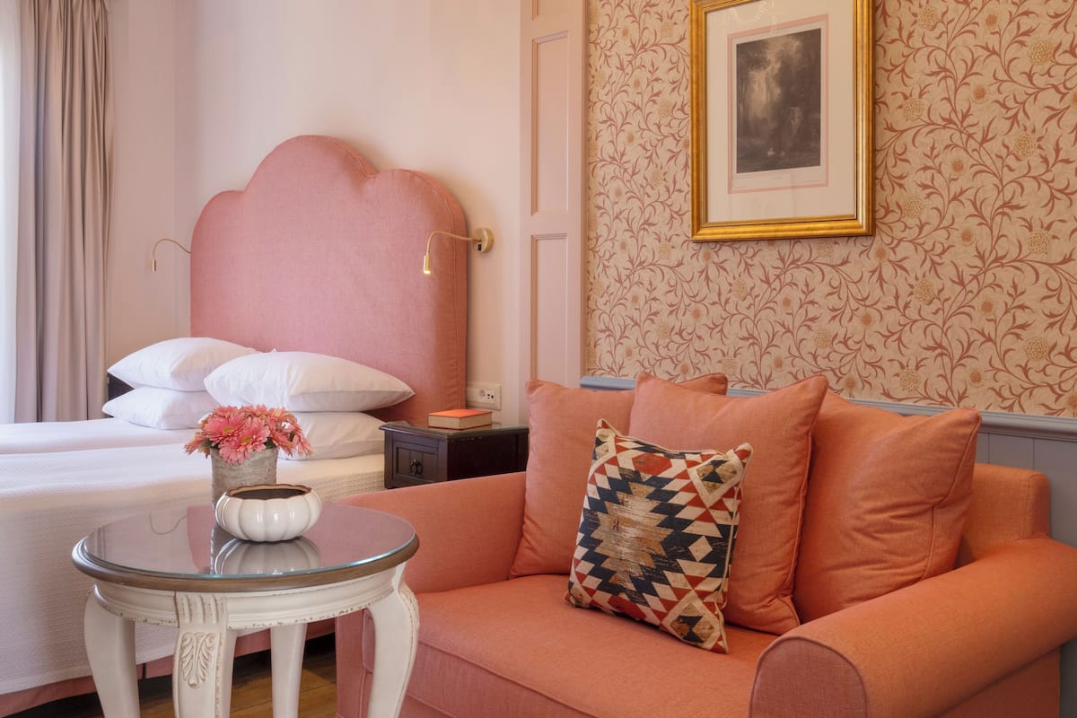 A bedroom with a bed, a nightstand, a table with a vase of flowers, and a sofa with patterned pillows.