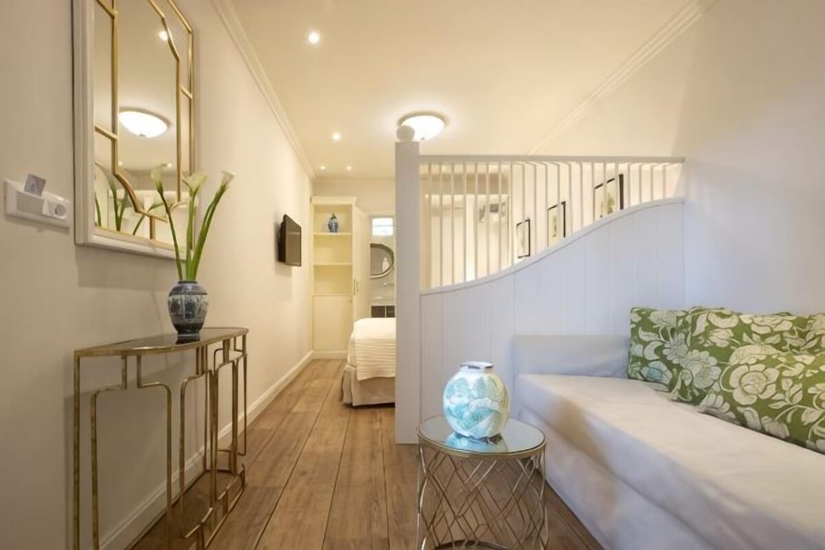 A hallway with a white sofa, a round table with a vase, and a mirror on the wall.