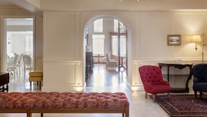 Ein geräumiges Wohnzimmer mit einer rot gepolsterten Bank, einer Chandelierleuchte und Blick in den Essbereich.