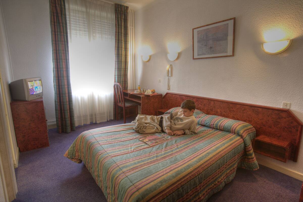 A hotel room with a bed, a desk, a chair, a telephone, and a television.