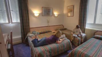 A room with three beds, a window with curtains, and two wall-mounted lamps.
