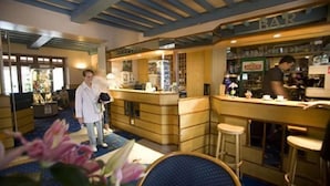 A bar area with wooden counters and stools, a person working behind the bar, and a visible liquor display.