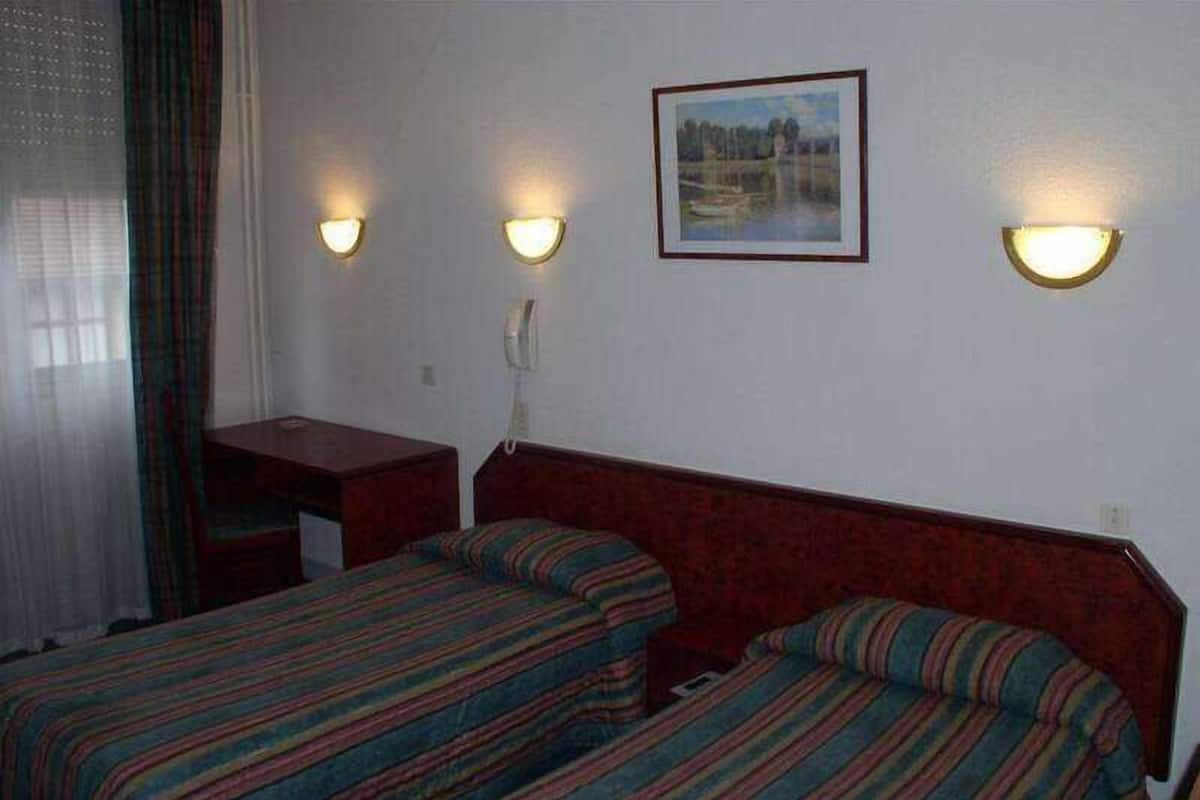 A hotel room with two single beds, a desk, and a telephone.